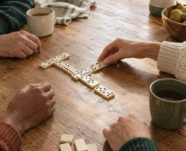 Former housemates playing dominoes around a kitchen table, with faces outside the frame.